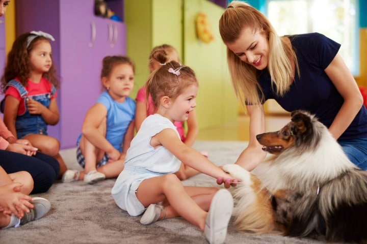 Happy children playing with dog supervised by a woman